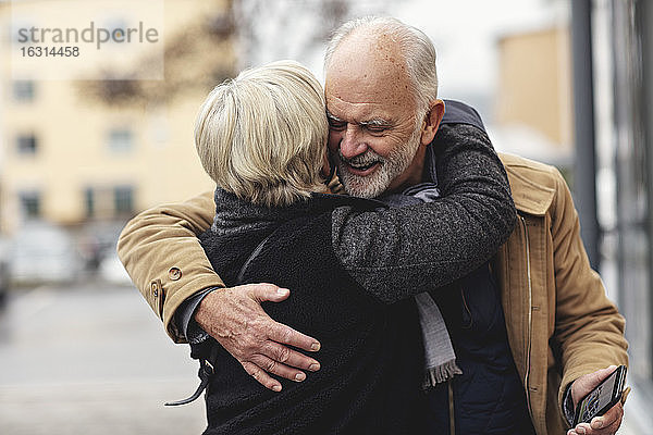 Lächelnder älterer Mann umarmt Partner während des Winters in der Stadt