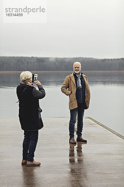 Ältere Frau in voller Länge fotografiert männlichen Partner am Seeufer bei klarem Himmel