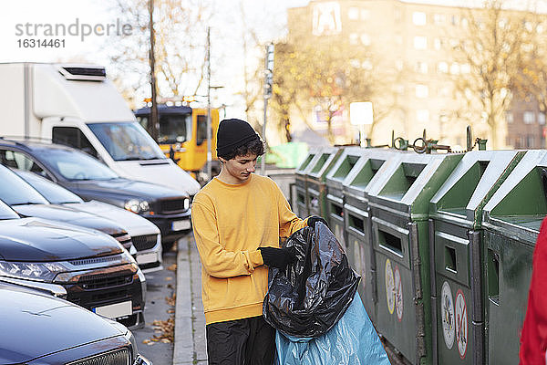Junger männlicher Freiwilliger hält Abfall in Plastiktüte an der Mülltonne