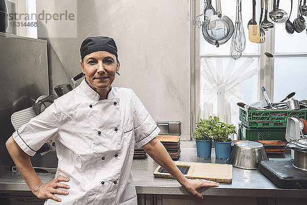 Porträt eines selbstbewussten reifen Küchenchefs mit der Hand auf der Hüfte in der Großküche