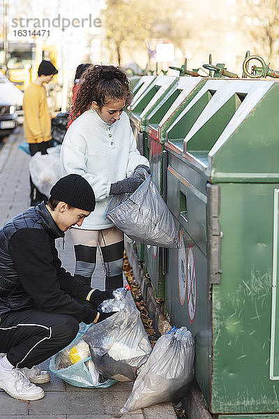 Junge männliche und weibliche Umweltschützer werfen Recycling-Müll in den Mülleimer