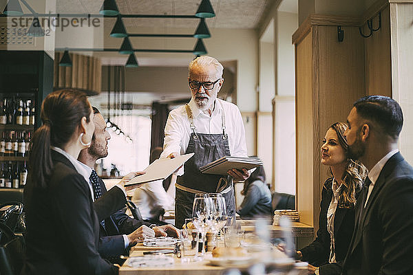 Kellner gibt Geschäftsleuten im Restaurant das Menü