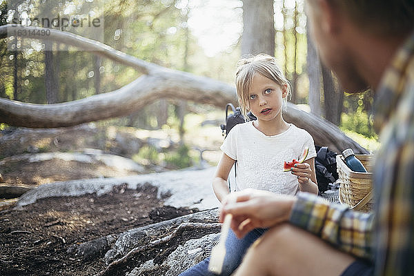 Tochter isst Wassermelone  während sie den Vater im Wald anschaut
