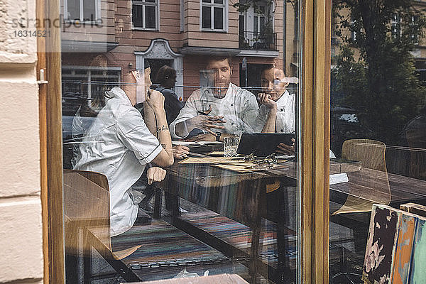 Männliche und weibliche Köche diskutieren am Restauranttisch durch ein Glasfenster gesehen