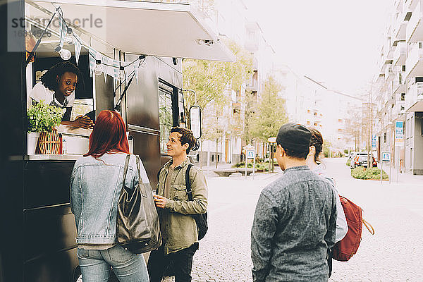 Besitzer mit Assistentin im Gespräch mit lächelnden Kunden per Speisewagen auf der Straße