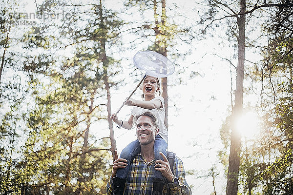 Lächelnder Vater trägt glückliche Tochter auf der Schulter beim Waldspaziergang