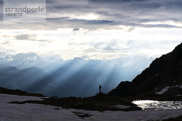 Silhouette eines einsamen Wanderers  der in der Morgendämmerung die Sonnenstrahlen über dem Zana-See bewundert  Valmalenco  Valtellina  Lombardei  Italien  Europa