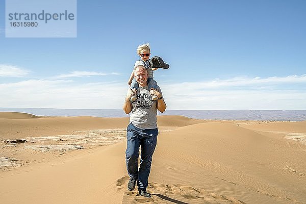 Vater geht mit huckepack 2 Jahre altem Sohn durch Sahara-Wüste in Marokko