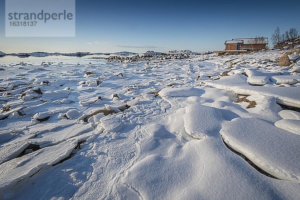 Holzhaus am Strand  gefrorener Fjord mit Eisschollen in Winterlandschaft  Nordland  Lofoten  Norwegen  Europa