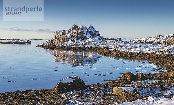 Verschneite winterliche Bucht mit Seegras bei Ebbe  blaues Meer  Holzhaus auf Felsinsel  Nordland  Lofoten  Norwegen  Europa