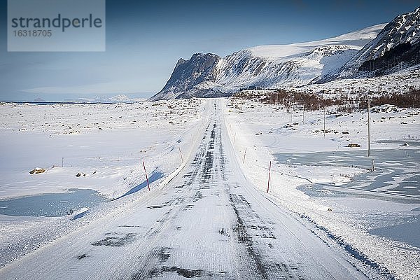 Vereiste Schneefahrbahn  in winterlicher Landschaft  hinten Bergkette und Meer  Nordland  Lofoten  Norwegen  Europa