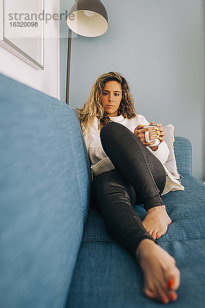 Porträt einer jungen Frau  die sich mit Kaffee auf dem Sofa entspannt