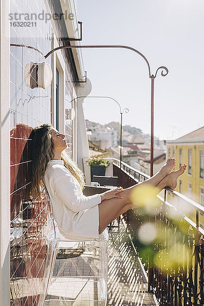 Gelassene junge Frau entspannt sich auf dem sonnigen Balkon ihrer Wohnung  Lissabon  Portugal