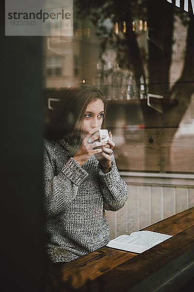 Junge Frau trinkt Kaffee und liest ein Buch am Fenster eines Cafés