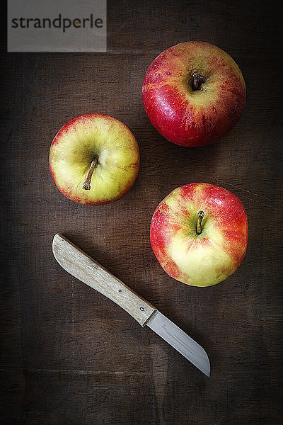 Drei Äpfel und Küchenmesser auf dunklem Holz