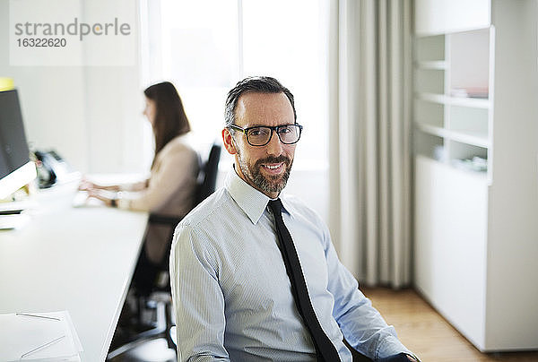 Porträt eines selbstbewussten Geschäftsmannes im Büro mit einem Angestellten im Hintergrund