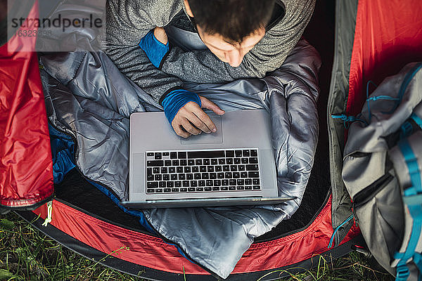 Mann zeltet in Estland  sitzt im Zelt und benutzt einen Laptop