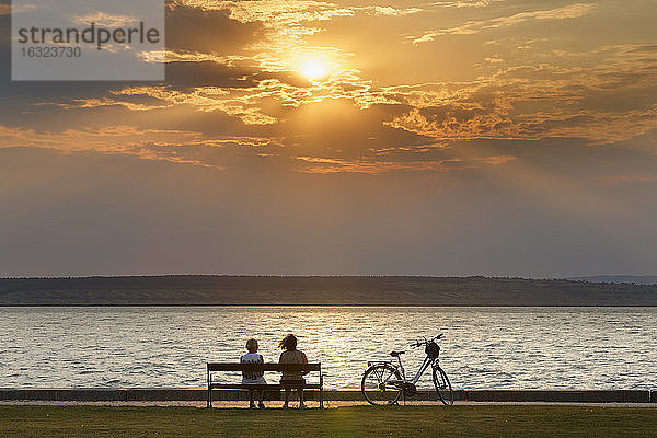 Österreich  Burgenland  Illmitz  Neusiedler See  Menschen auf Bank sitzend bei Sonnenuntergang