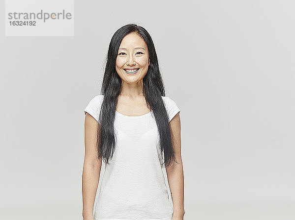 Porträt einer lächelnden Frau mit langen schwarzen Haaren und weißem Hemd