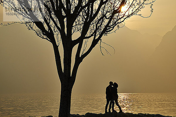 Italien  Torbole  Gardasee  Paar küsst sich am Seeufer in der Abenddämmerung