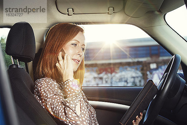 Rothaarige Geschäftsfrau sitzt in ihrem Auto und telefoniert mit ihrem Smartphone