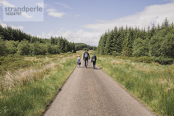 Rückenansicht eines Vaters  der mit seinen Söhnen auf einer Landstraße wandert  Cairngorms  Schottland  UK