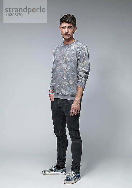Porträt eines jungen Mannes in einem gemusterten Pullover vor grauem Hintergrund