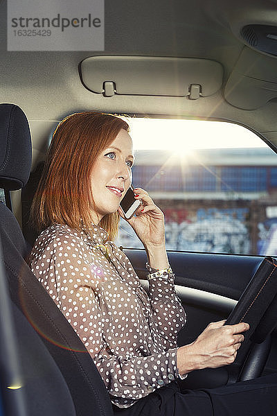 Rothaarige Geschäftsfrau sitzt in ihrem Auto und telefoniert mit ihrem Smartphone