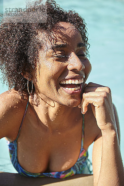 Lachende junge Frau  die am Pool lehnt