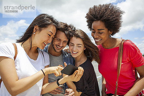 Glückliche junge Freunde beim Betrachten von Fotos auf dem Smartphone
