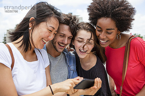 Glückliche junge Freunde beim Betrachten von Fotos auf dem Smartphone