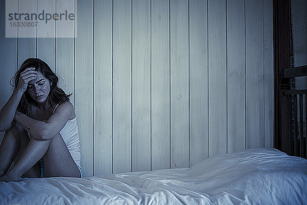 Traurige junge Frau auf dem Bett sitzend
