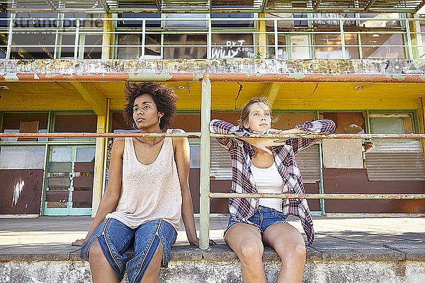 Junge Freundinnen sitzen in der Nähe von Geländern im Freien