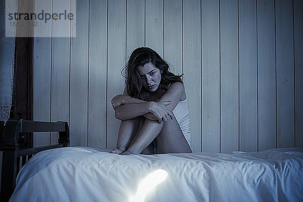 Traurige junge Frau auf dem Bett sitzend