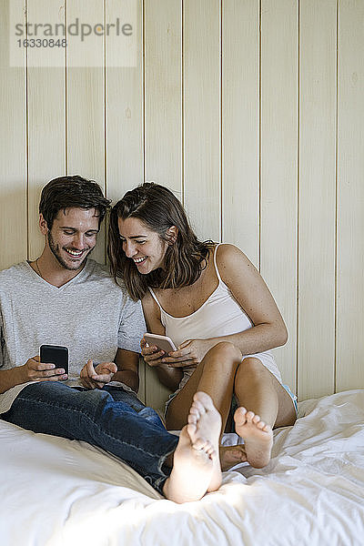 Junges Paar benutzt Smartphones im Schlafzimmer