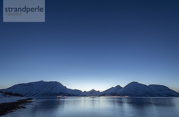 Winterlich verschneite Bergkette über dem Meer  arktische Winterlandschaft  darüber Nachthimmel mit Sternen