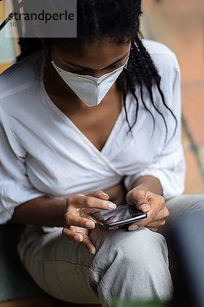 Junge schwarze Frau mit Gesichtsmaske  die ein Smartphone benutzt