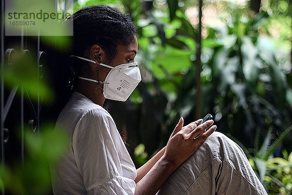 Junge schwarze Frau mit Gesichtsmaske  die ein Smartphone benutzt