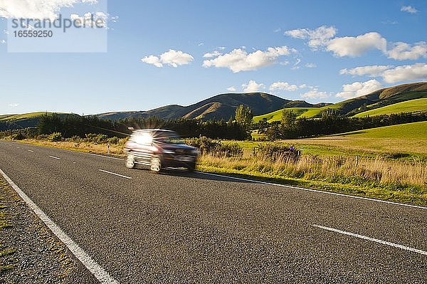 Auto mit überhöhter Geschwindigkeit auf einer Straße auf der Südinsel Neuseelands. Dieses Foto wurde in der Region Central Otago auf der Fahrt zwischen Christchurch und Lake Tekapo aufgenommen. Die Landschaft auf der Südinsel Neuseelands ist so vielfältig  aber immer schön. In der einen Minute leuchtend grüne  grasbewachsene Hügel  in der nächsten schneebedeckte Berge.