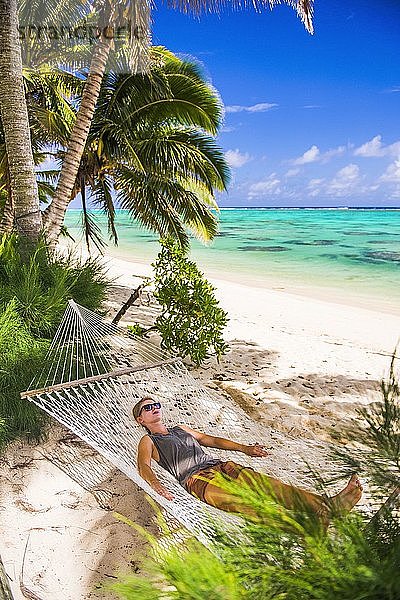 Frau entspannt sich in einer Hängematte unter Palmen am weißen Sandstrand auf der tropischen Insel Rarotonga  Cookinseln  Südpazifik