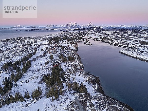 Luftaufnahme winterliche Insellandschaft im Abendlicht vor der Küste  hinten hohe Berggipfel  Dønna  Nordland  Norwegen  Europa