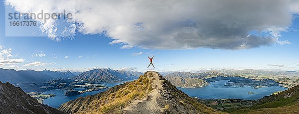 Wanderer macht einen Luftsprung  Ausblick auf Berge und See vom Mount Roy  Roys Peak  Lake Wanaka  Südalpen  Otago  Südinsel  Neuseeland  Ozeanien