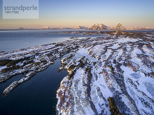 Luftaufnahme winterliche Insellandschaft im Abendlicht vor der Küste  hinten hohe Berggipfel  Dønna  Nordland  Norwegen  Europa