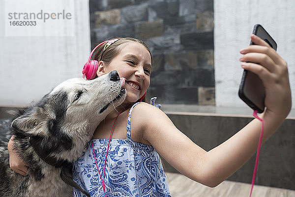 Mädchen nimmt Selfie mit Hund durch Mobiltelefon zu Hause