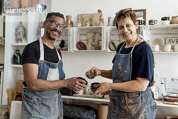 Lächelnde Mitarbeiter  die in der Werkstatt stehen und Keramiken halten