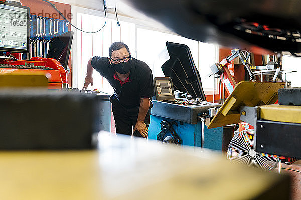 Mechaniker mit Maske schaut bei der Arbeit in einer Autowerkstatt weg