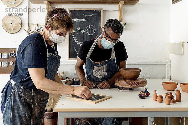 Mitarbeiter mit Masken besprechen Entwürfe auf einem Schiefertisch in einer Werkstatt