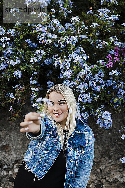 Lächelnde junge Frau  die Blumen hält  während sie gegen Pflanzen im Park steht