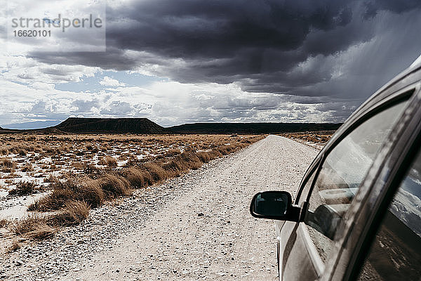 Spanien  Navarra  Gewitterwolken über einem Auto auf einem leeren Feldweg in Bardenas Reales