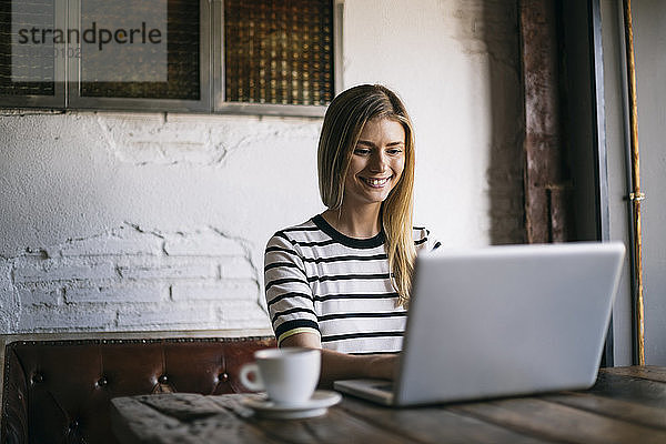Mittlere erwachsene Frau lächelt bei der Benutzung eines Laptops in einem Cafe